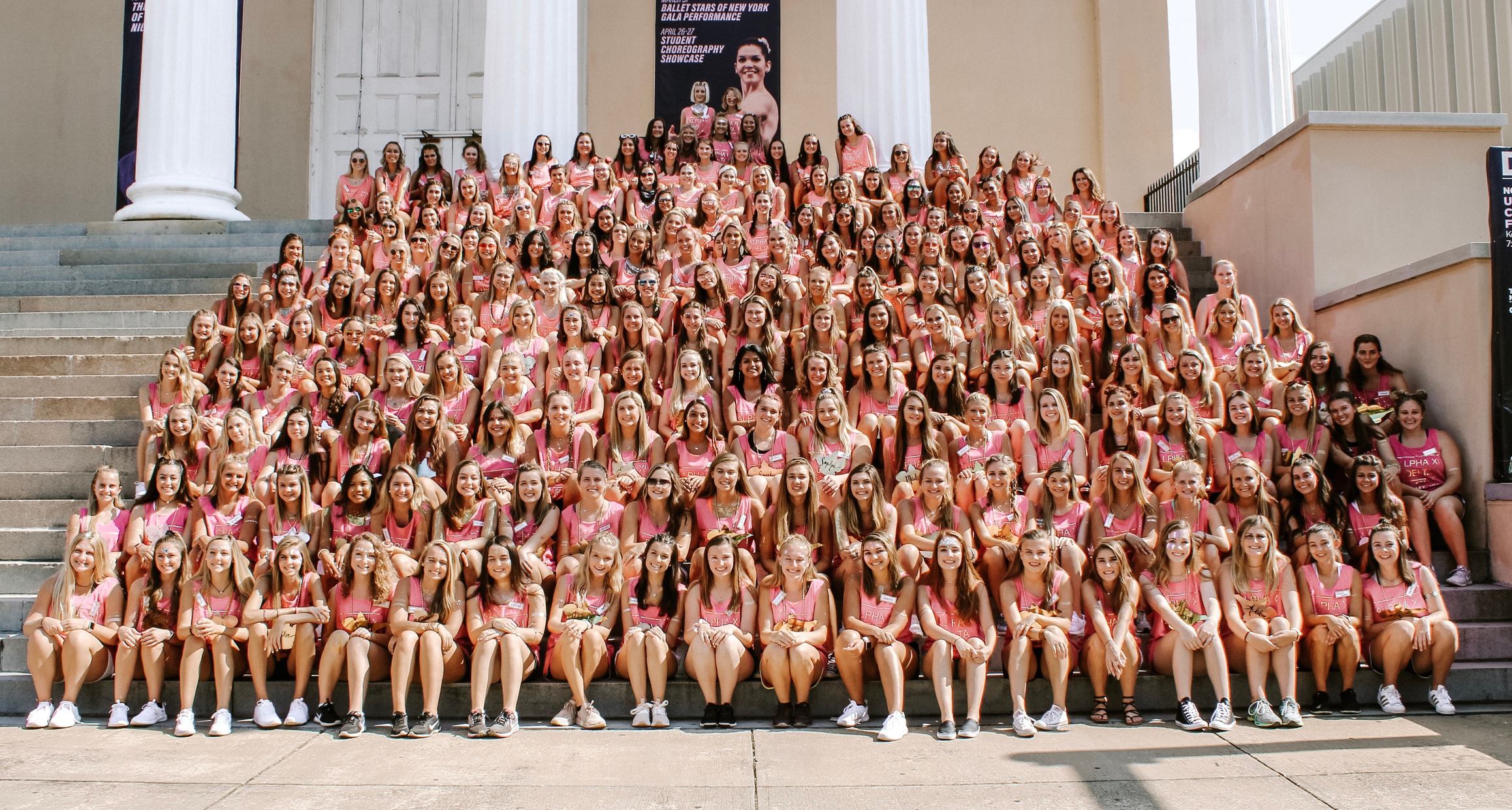 a large group of sorority members in pink shirts sitting on steps in front of a building