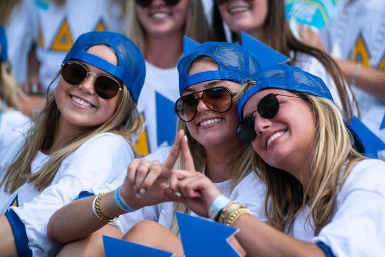 A group of sorority women celebrating bid day wearing blue and white hats and sunglasses.