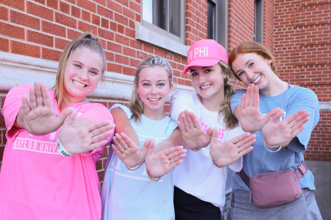 four individuals wearing pink shirts and holding up their hands to sorority symbols